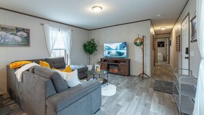 A modern living room with a grey sofa, a flat-screen TV, a fireplace, and a hallway leading to another room. - Sky Lodge House - 3BR+BBQ - 5 min to BZN Airport (Belgrade)