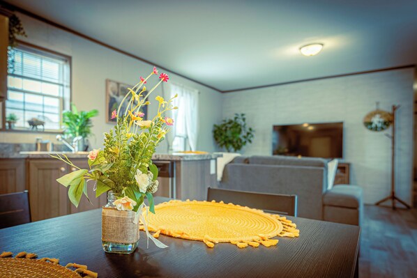 A dining table with a placemat, a vase with flowers, and a woven placemat on the floor.