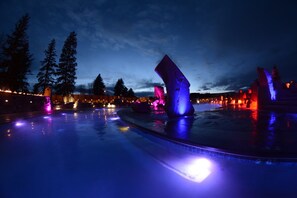 A swimming pool with illuminated sculptures and trees in the background.