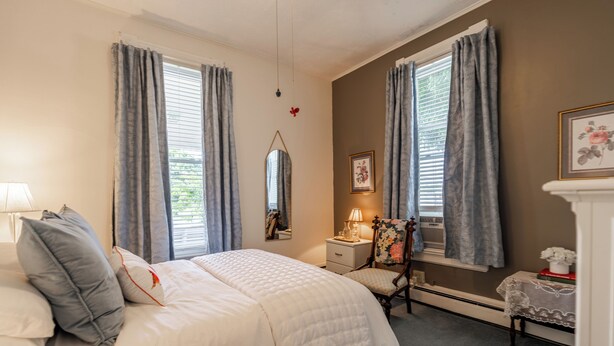 Une chambre à coucher comprenant un lit, une table de chevet, une lampe, une chaise, un miroir et une petite table sur laquelle est posé un vase.