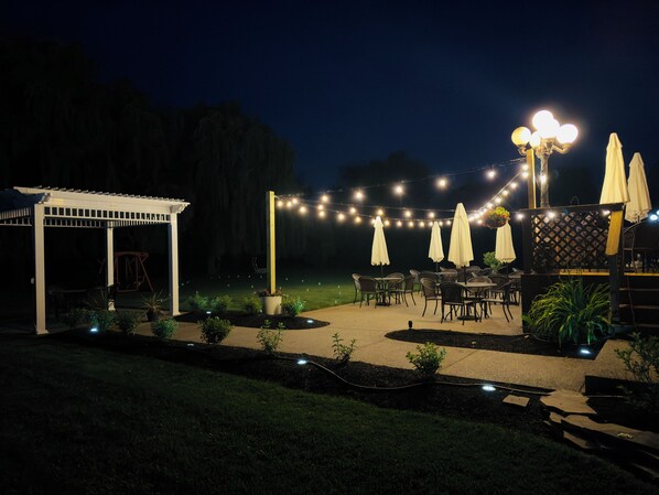 Un patio al aire libre con luces colgantes, sombrillas y mesas.