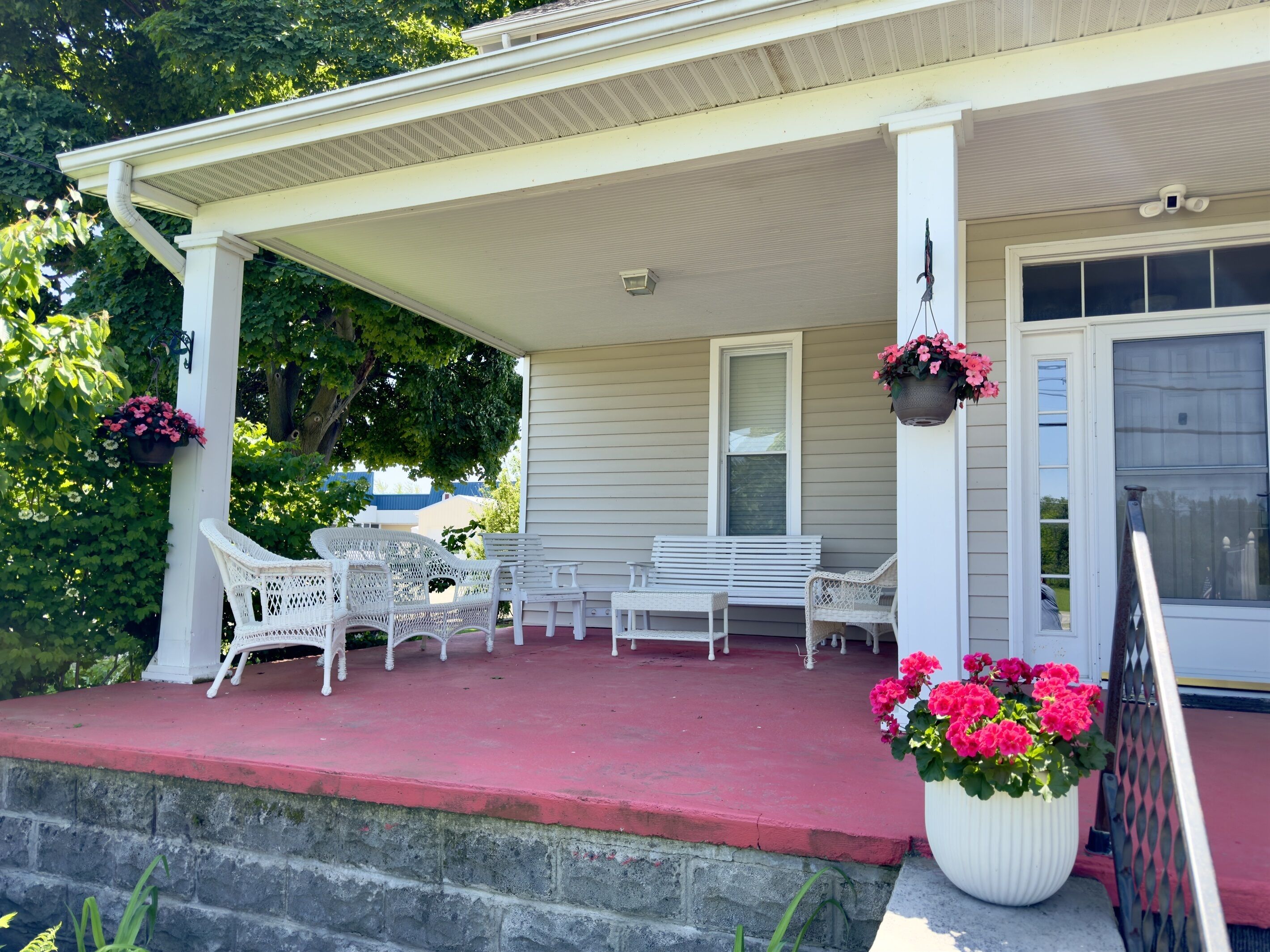 A covered porch with white wicker furniture and a red floor.