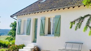 Ein weißes Gebäude mit einem Ziegeldach, grünen Fensterläden und einer Bank davor.