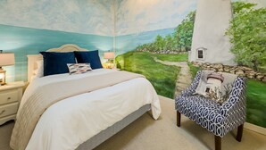 Un dormitorio con un mural de un faro, una cama con ropa de cama azul y blanca, y un sillón con estampado.