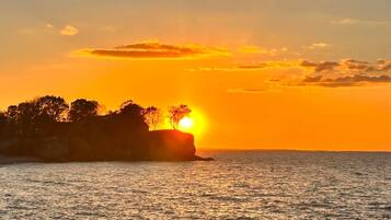 Un coucher de soleil sur une étendue d’eau, avec en silhouette des arbres et une falaise.