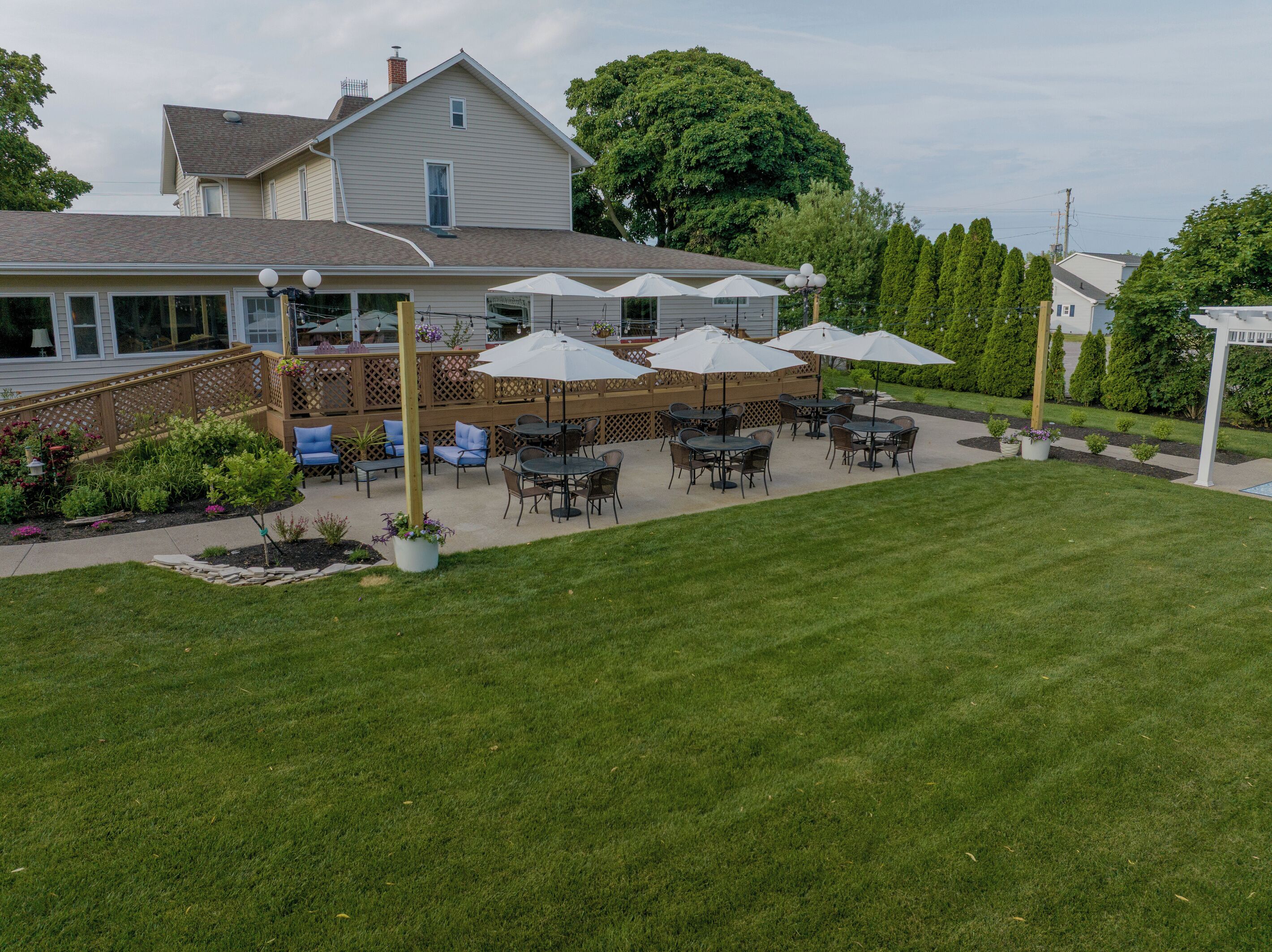 A patio area with outdoor seating and umbrellas, surrounded by a well-maintained lawn and garden.