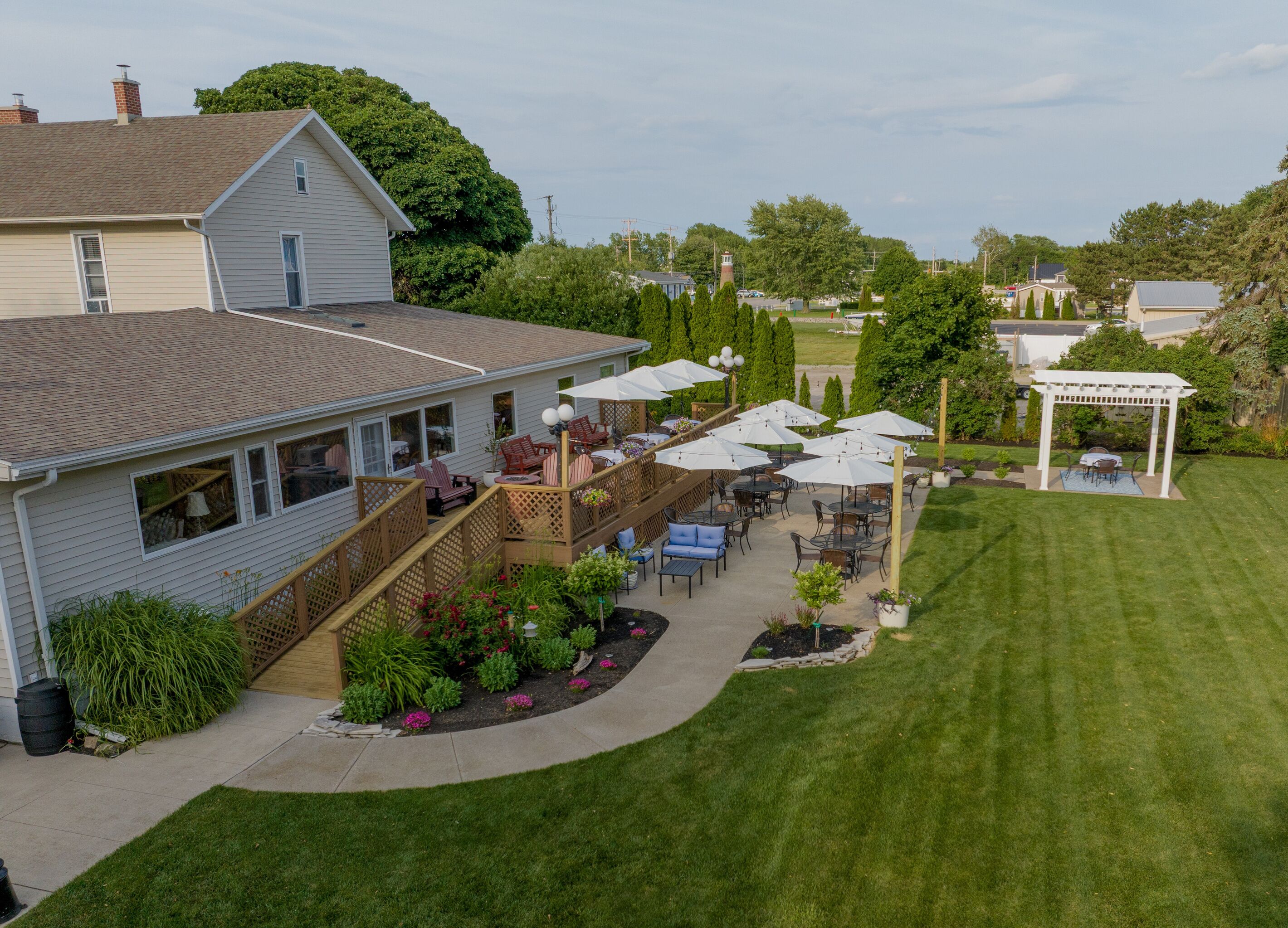 A house with a patio area featuring outdoor furniture and umbrellas, surrounded by a well-maintained lawn and garden.