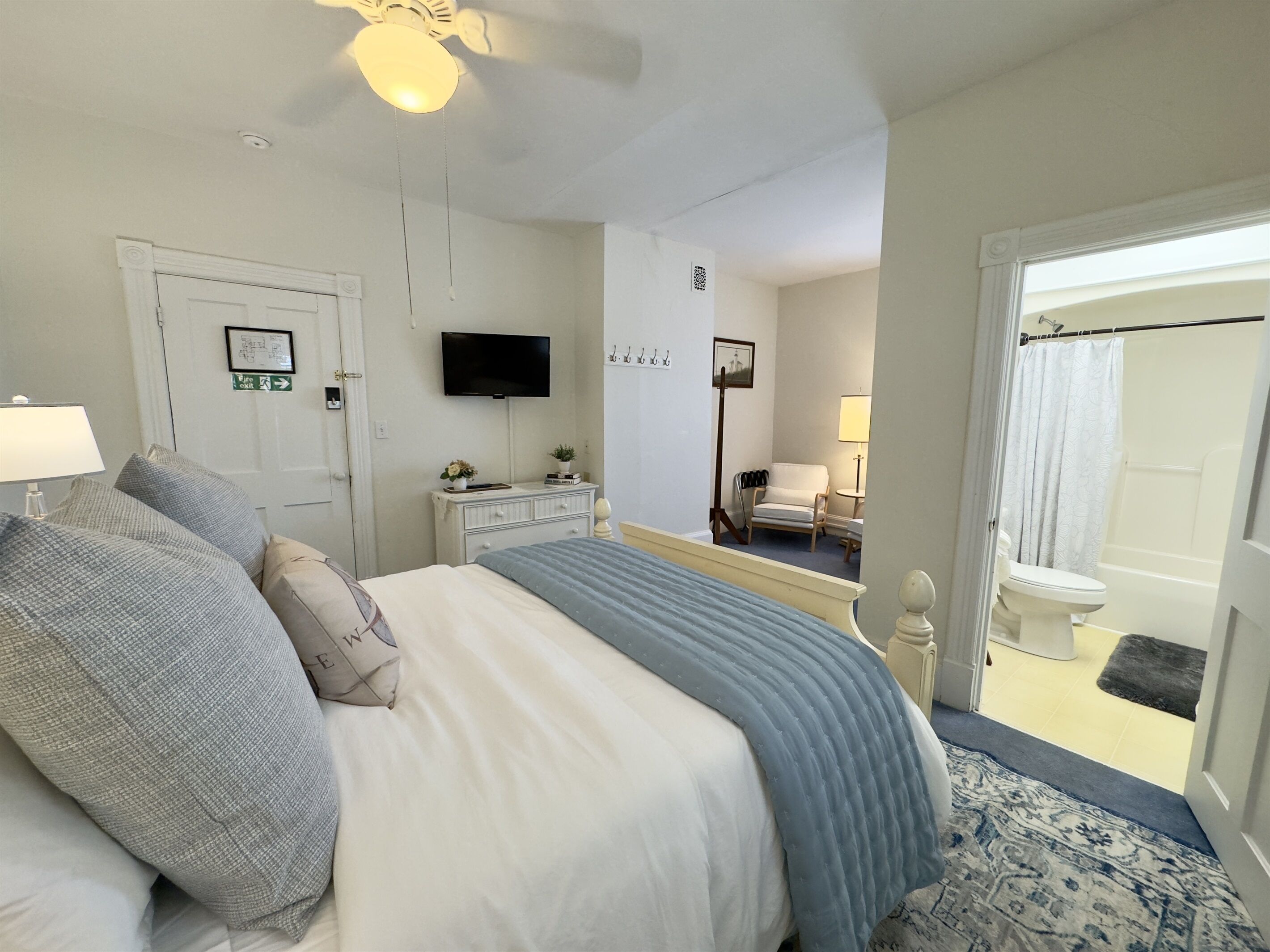 Een slaapkamer met een bed, een dressoir, een televisie, een stoel en een badkamer zichtbaar door een geopende deur.