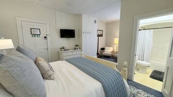 Een slaapkamer met een bed, een dressoir, een televisie, een stoel en een badkamer zichtbaar door een geopende deur.