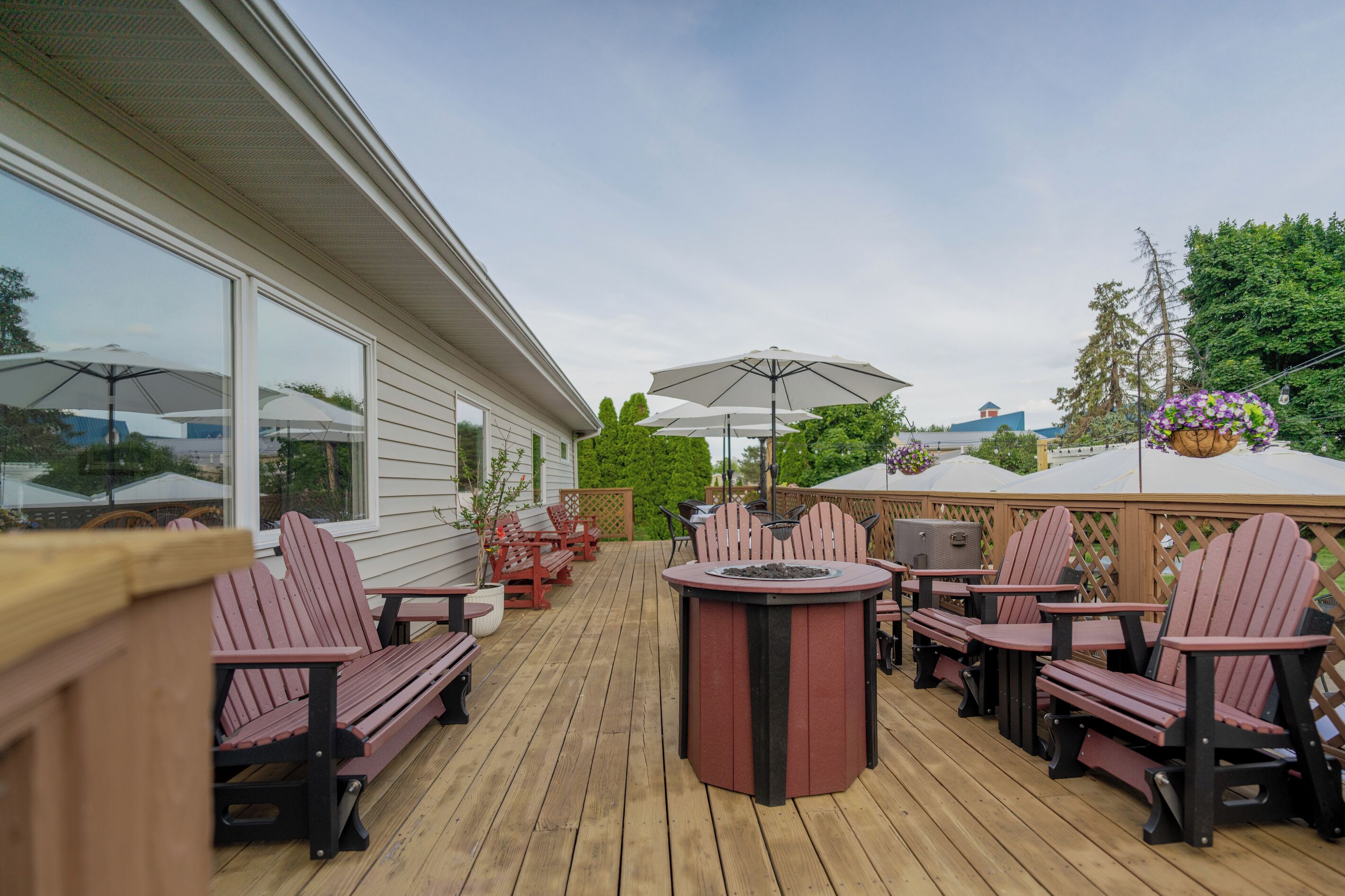 A wooden deck with Adirondack chairs, a round table, and umbrellas.