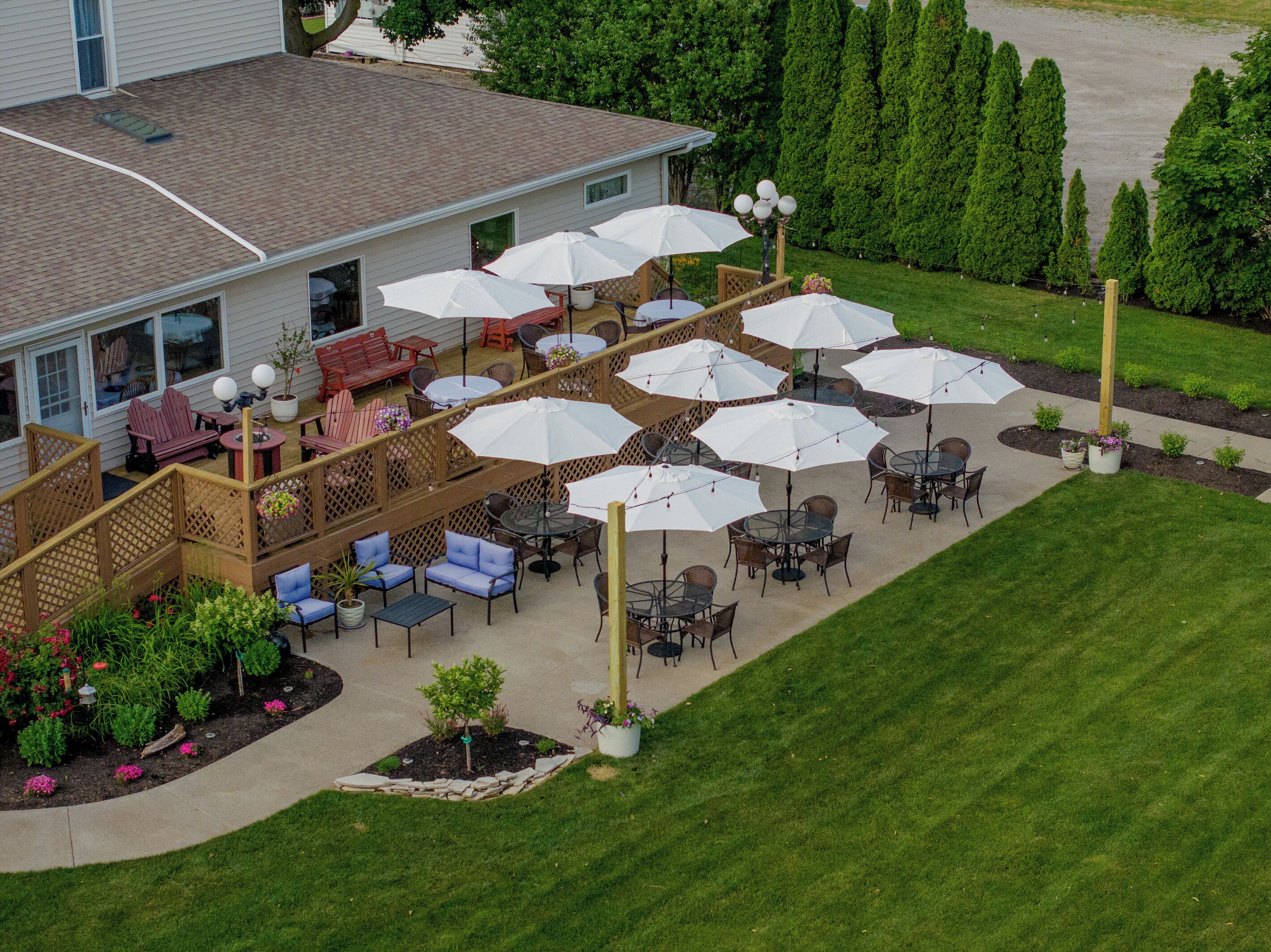 A patio area with outdoor seating and umbrellas, surrounded by a wooden deck and a lawn.