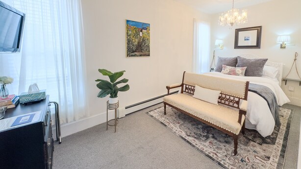 A bedroom with a bed, bedside lamps, a chandelier, a painting, and a potted plant. - Relaxing Couples Retreat Near Lake Erie (Lakeside-Marblehead)