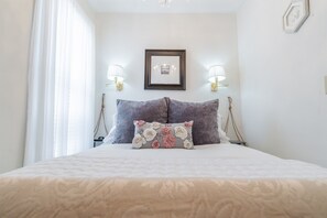 A neatly made bed with a floral pillow, two wall-mounted lamps, and a framed picture on the wall. - Relaxing Couples Retreat Near Lake Erie (Lakeside-Marblehead)
