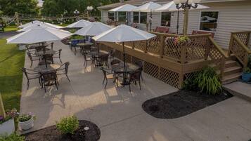 An outdoor patio area with tables and chairs, umbrellas, and a wooden deck.