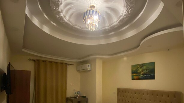 Ein Hotelzimmer mit einem großen Bett, einer Decke mit einem Chandelier, einem Gemälde an der Wand und einer Klimaanlage.