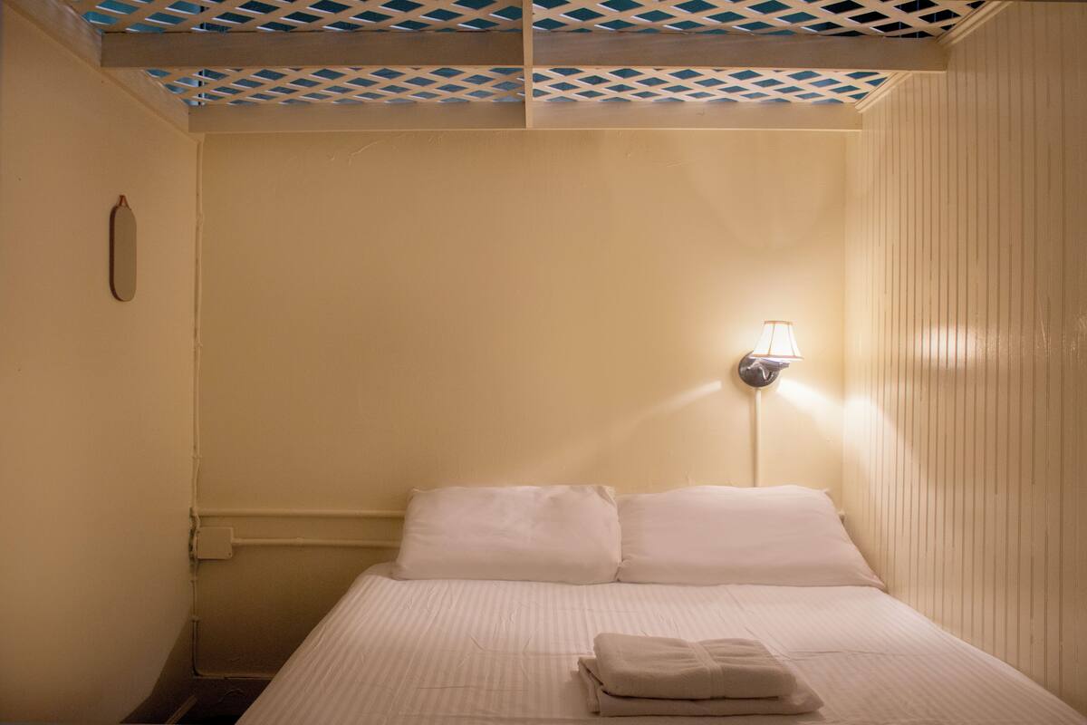 A hotel room with a bed, a wall-mounted lamp, and a patterned ceiling.
