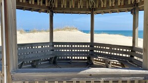 Um gazebo de madeira à beira-mar com vista para o oceano e dunas de areia.