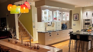 Una cucina moderna con mobili bianchi, un'isola centrale con sgabelli da bar e una scala che conduce a un altro piano.