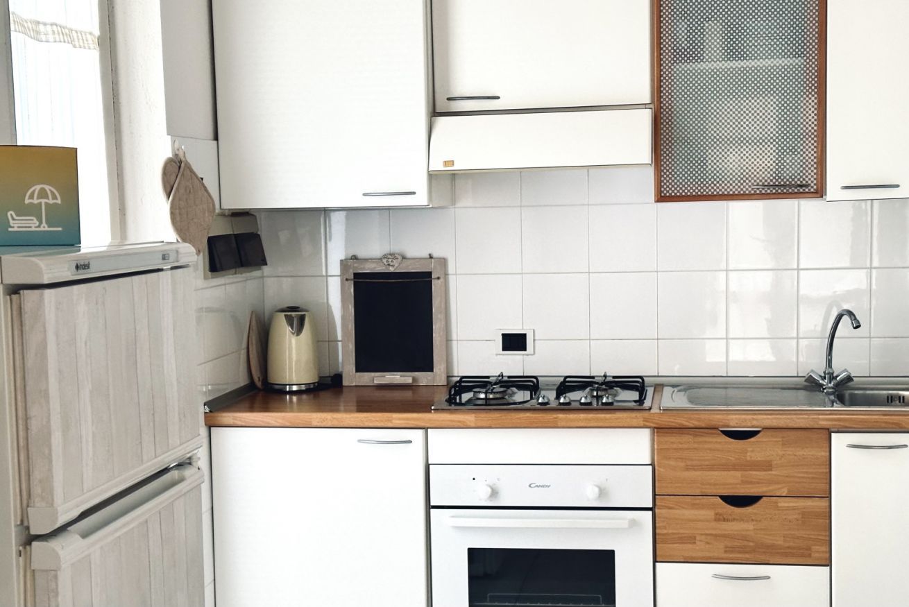 Moderni keittiö, jossa on valkoiset kaapit, puinen työtaso, kaasuliesi, vedenkeitin ja pesuallas.