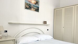 A bedroom with a bed, a nightstand, a wall-mounted shelf, a picture, and a wardrobe. - N289 - Numana, two-room apartment with garden (Numana)