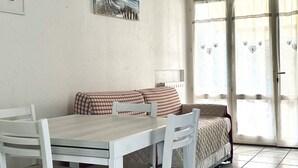 A dining area with a table and chairs, a sofa with a checkered blanket, and a sliding glass door with heart-patterned curtains. - N289 - Numana, two-room apartment with garden (Numana)