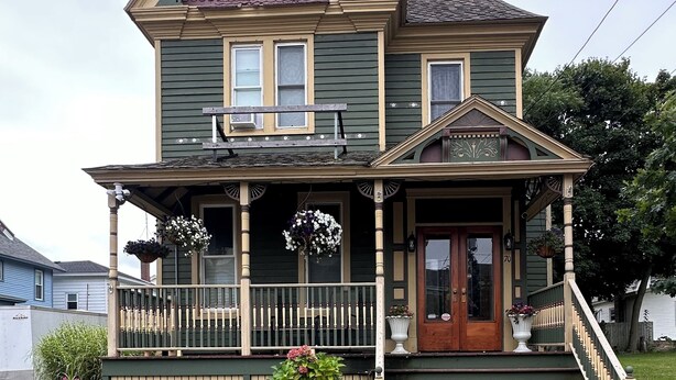 A two-story Victorian-style house with a front porch, a staircase, and a brick foundation.