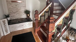 A staircase with wooden balusters and a handrail, leading to a landing with a stone wall and a black rug.