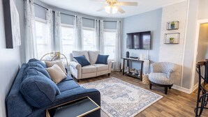 A living room with a blue sofa, a beige armchair, a patterned rug, and a wooden floor.