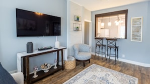 A living room with a TV, a console table with decorative items, a patterned rug, and a bar area with stools.