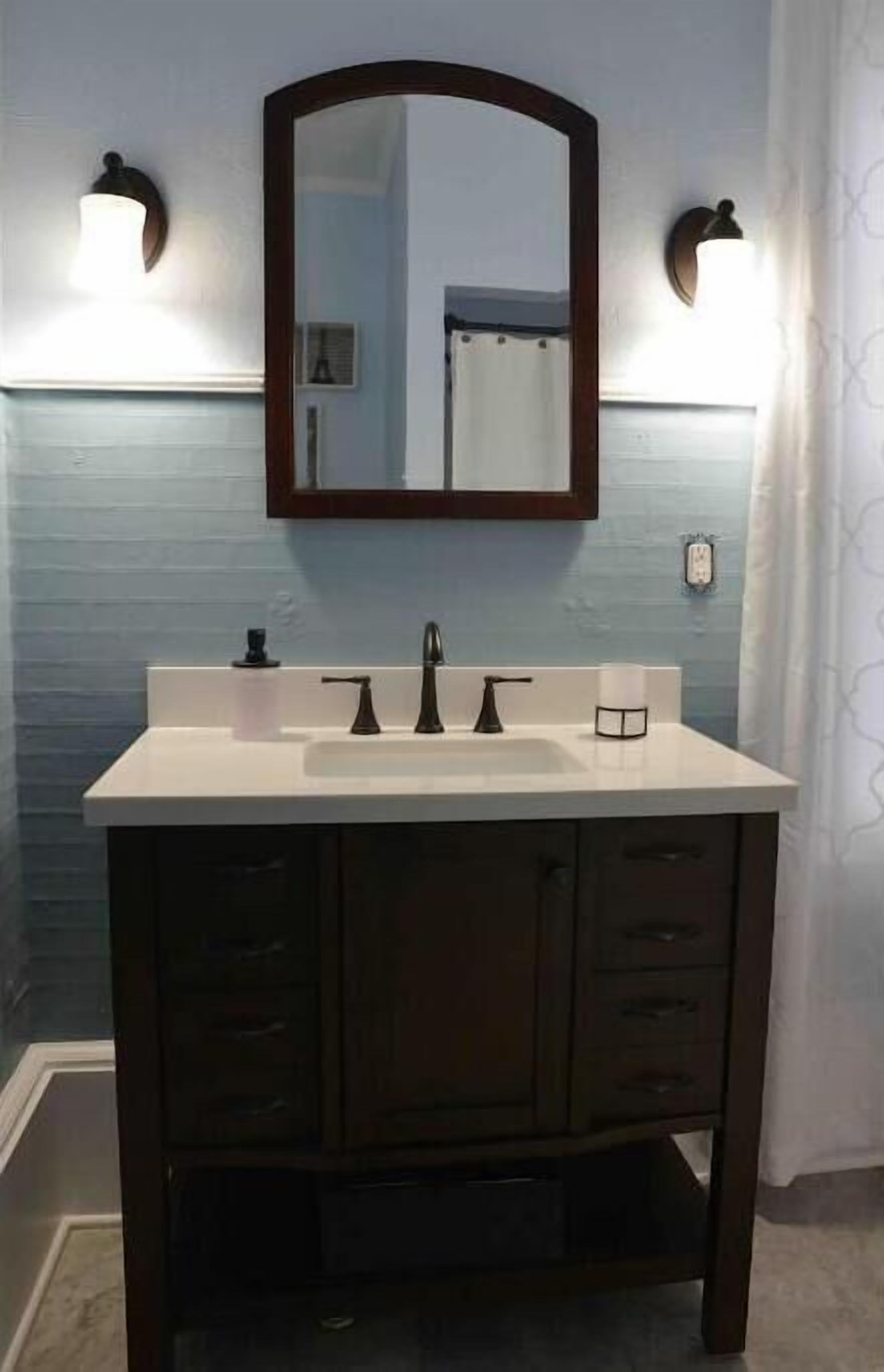 A bathroom with a white sink, dark wooden cabinets, and a mirror with two wall-mounted lights.