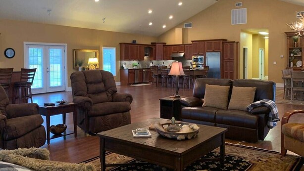 A spacious living room with a fireplace, a dining area, and a kitchen with wooden cabinets. - Grandview Acres Lodge (DeWitt)