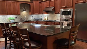 A kitchen with wooden cabinets, a granite island, bar stools, stainless steel appliances, and a backsplash. - Grandview Acres Lodge (DeWitt)