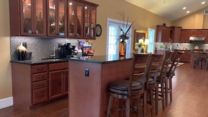 A spacious kitchen with wooden cabinets, a central island with bar stools, and a tiled backsplash. - Grandview Acres Lodge (DeWitt)