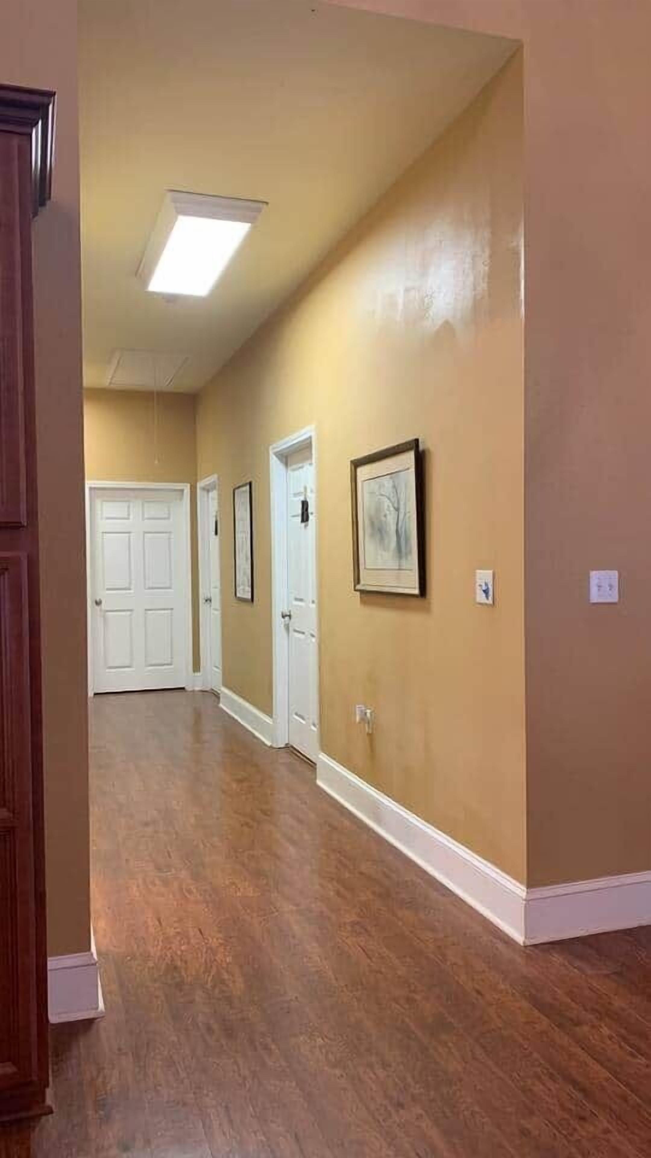 A hallway with wooden flooring, beige walls, and white doors.