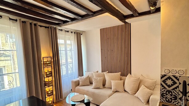 A modern living room with a sectional sofa, a coffee table, and a dining area with a black table. - Charming Apartment in Center Paris (Paris)