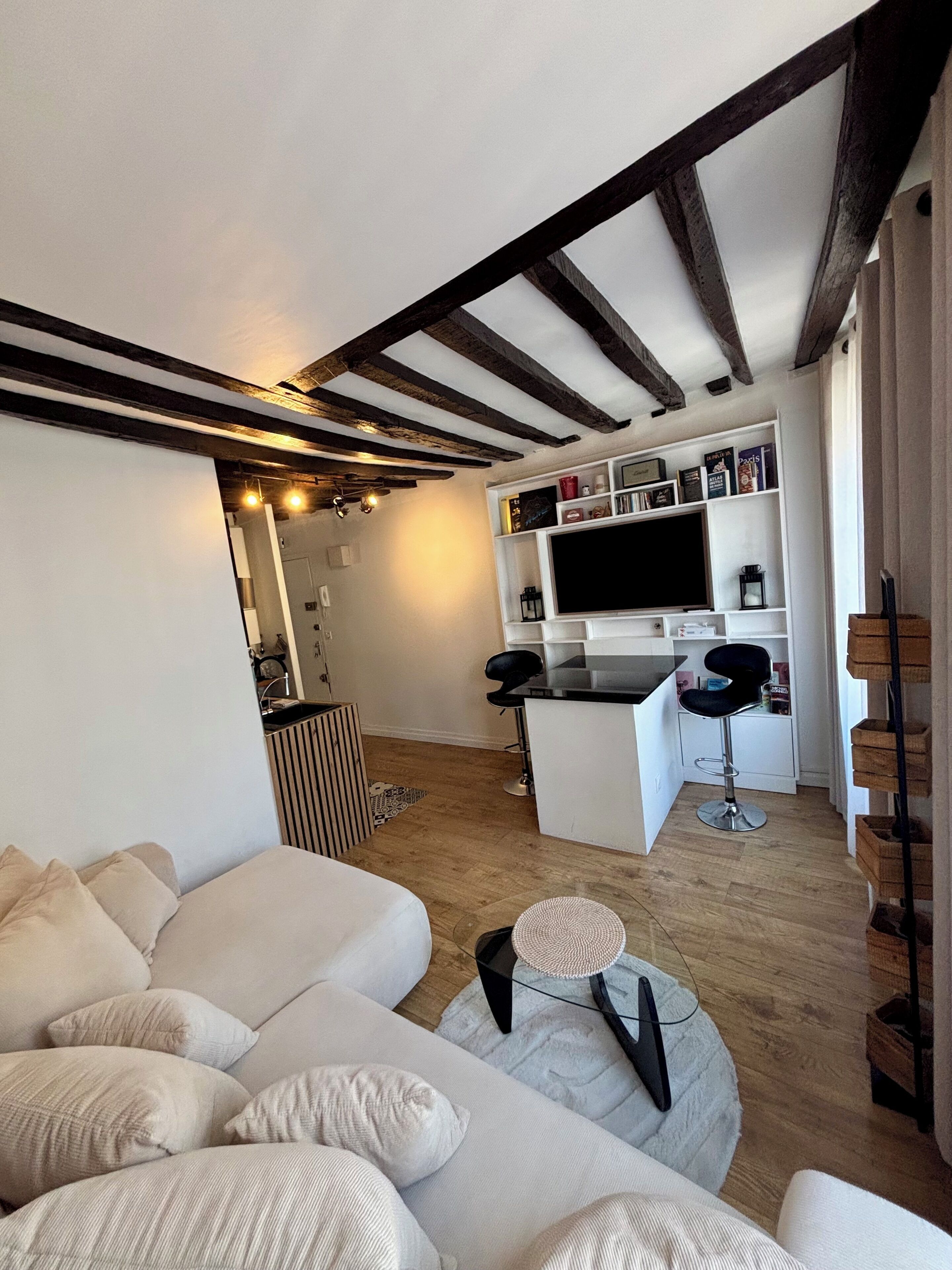 Un salon moderne comprenant un canapé, une table basse et un coin cuisine avec un téléviseur et des tabourets de bar.