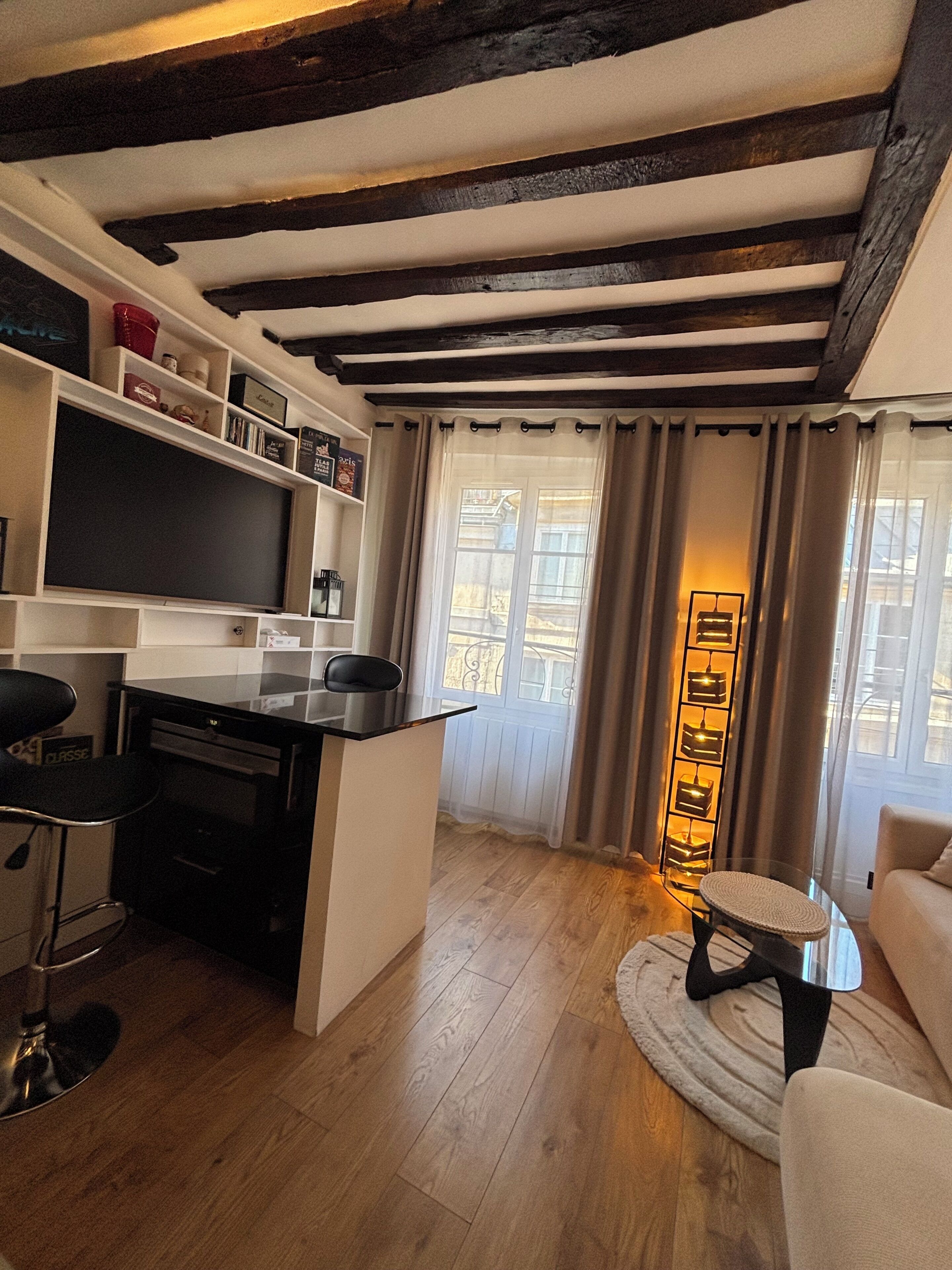 A modern living room with a kitchen area, wooden flooring, and a black-framed TV.