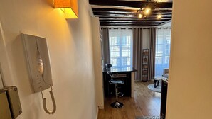 A narrow hallway with wooden flooring, a telephone on the wall, and a patterned rug. - Charming Apartment in Center Paris (Paris)