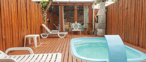A wooden deck with a hot tub, lounge chairs, and a covered seating area.