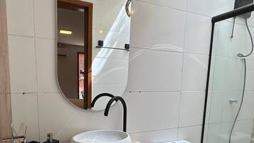 A modern bathroom with a round mirror, a sink, a toilet, and a glass-enclosed shower.