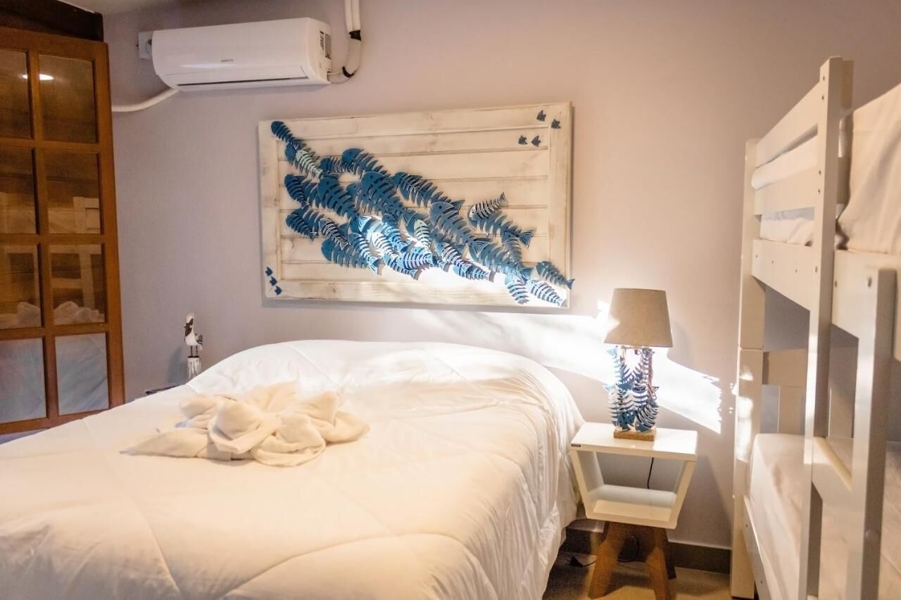 Een net opgemaakt bed met een witte dekbedovertrek en een opgevouwen handdoek. Daarboven hangt een wandairco en op de muur een decoratief kunstwerk van een blauwe varen.