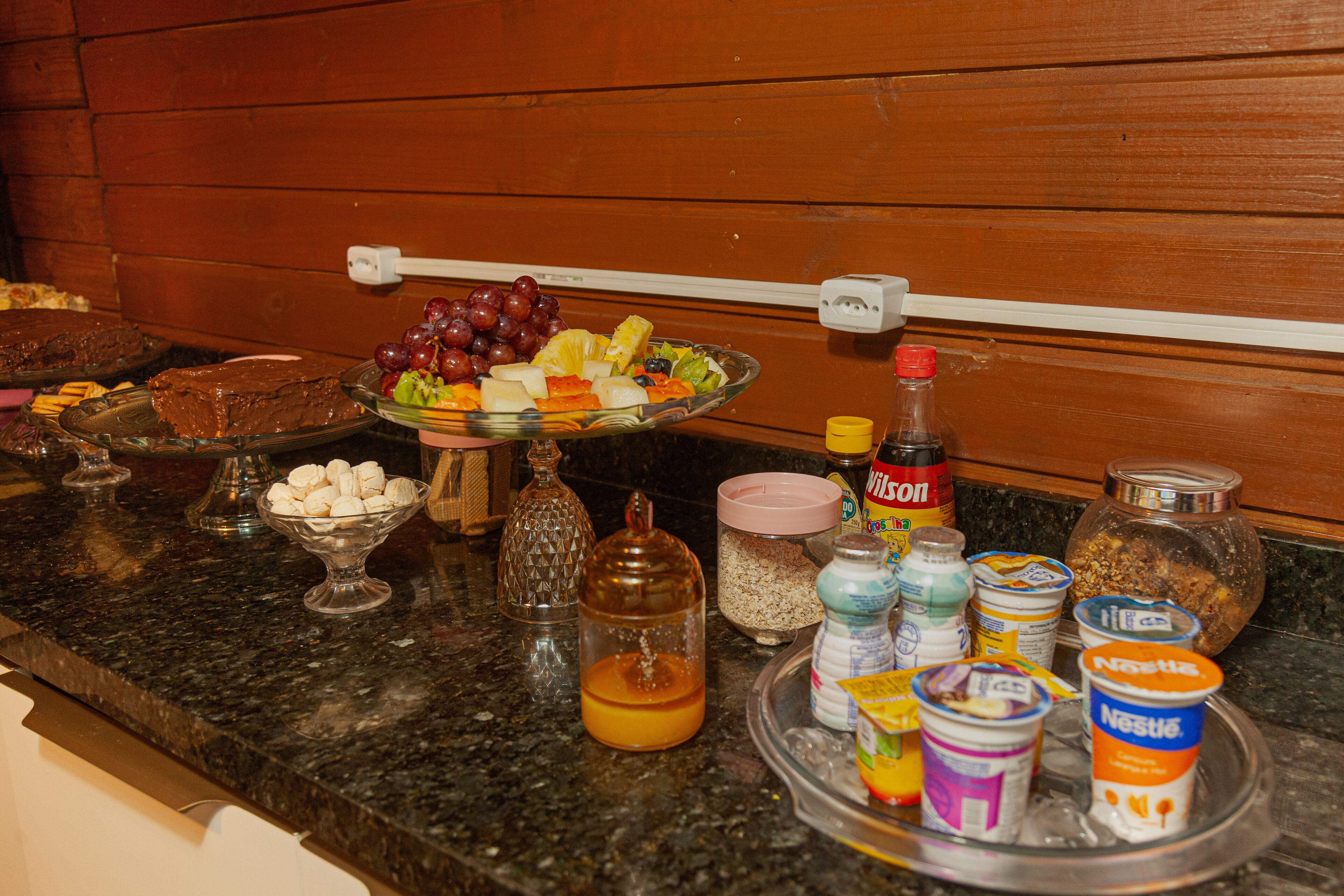 A kitchen counter with various food items, including a fruit bowl, a glass jar, and several containers of yogurt.