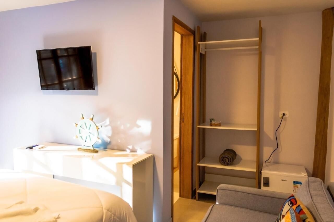 A bedroom with a bed, a desk with a chair, a TV mounted on the wall, and a wardrobe with shelves.