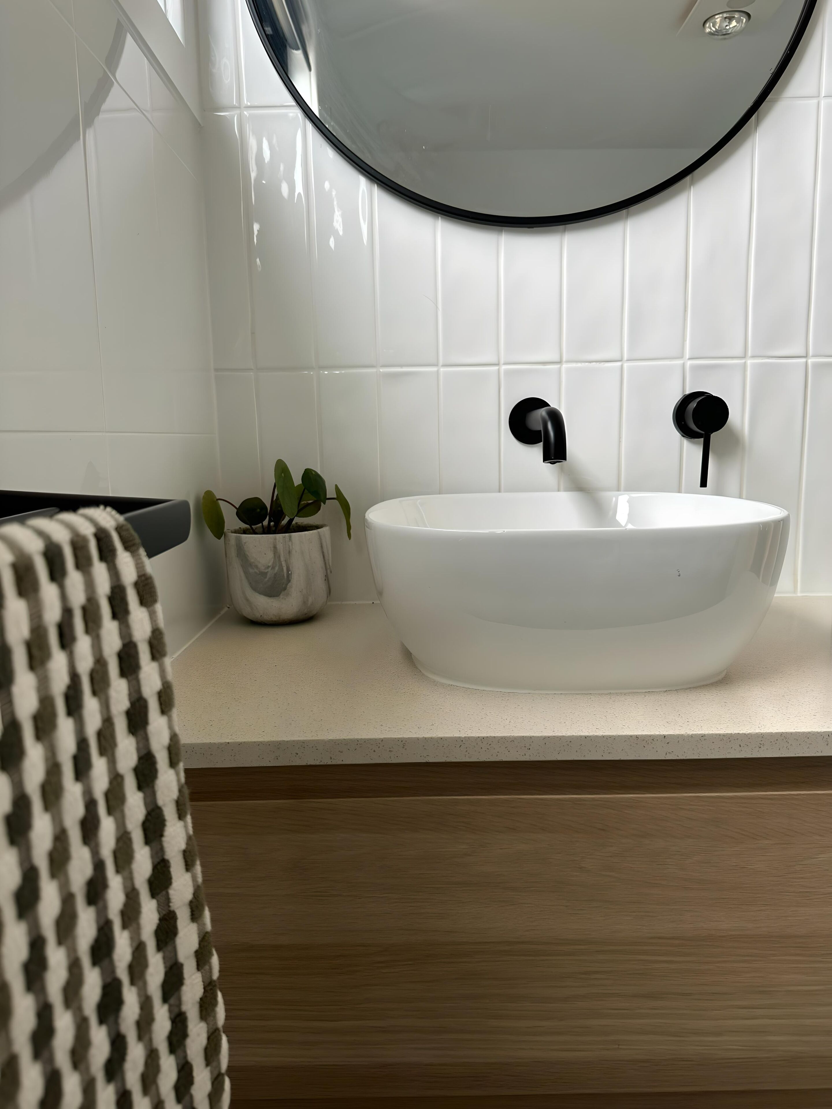 A bathroom with a white sink, black faucet, and a round mirror above it.