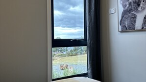 Une chambre avec une grande fenêtre, un lit recouvert d’une courtepointe à carreaux et un tableau encadré représentant des koalas accroché au mur.