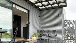 Une terrasse moderne avec une porte vitrée donnant sur une pièce, des chaises en métal noir, une table en bois et une plante en pot.
