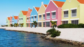 A row of colorful seaside houses with white balconies and a sandy beach in the background. - Corallium Hotel & Villas Bonaire (Kralendijk)