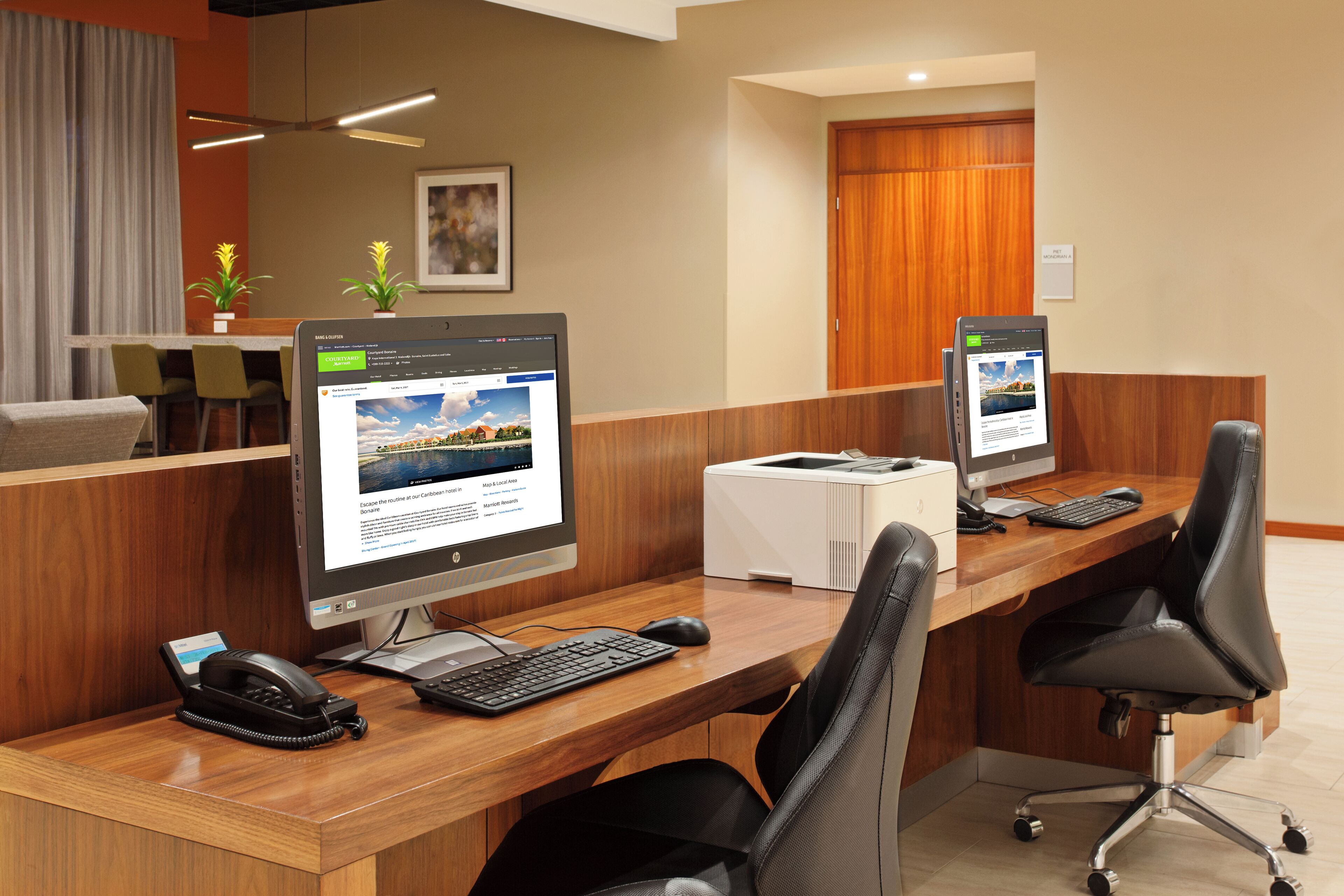 A modern office with two desktop computers, a printer, and a telephone on a wooden desk.