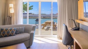 Quarto de hotel com sofá, escrivaninha e vista para a praia através de grandes portas de correr.