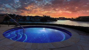 Piscina com vista para o pôr do sol sobre a água, cercada por casas.